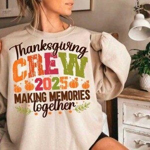以下が含まれることがあります： 「Thanksgiving CREW 2025 MAKING MEMORIES together」と書かれたカラフルなデザインの、かぼちゃと葉っぱが描かれたベージュのスウェットシャツ。秋の祝日にぴったりのカジュアルなトップスです。