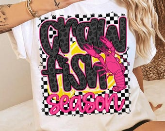 May include: White t-shirt with the words "CRAW FISH SEASON" in a playful font. The text is outlined in pink and black, with a leopard print pattern. A pink crawfish graphic is also included.