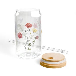 Puede incluir: Un vaso transparente en forma de lata con un diseño floral con flores rojas, amarillas y rosas. Incluye una pajita de cristal transparente y una tapa de madera con un inserto blanco. El vaso está diseñado para bebidas frías.