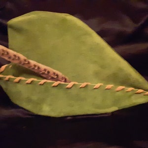 以下が含まれることがあります： 茶色の革の縁とステッチが付いた緑色のフェルトハット。帽子は半分に折り畳まれており、先のとがった先端があります。