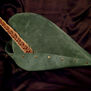 May include: A green suede hat with a brown feather and gold metal accents.