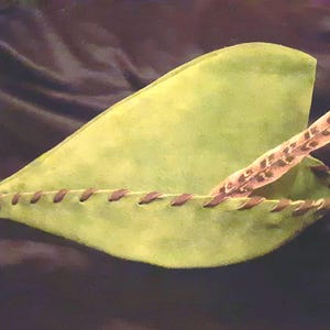 May include: A green felt hat with a brown feather trim. The hat has a pointed tip and a stitched seam around the brim.