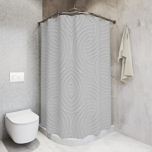 May include: A light gray shower curtain with a repeating, symmetrical pattern of curved lines and oval shapes. The curtain hangs from a curved metal rod in a corner shower. A white toilet is in the foreground.