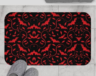 May include: A rectangular bath mat featuring a repeating pattern of red bats and swirling vine motifs set against a solid black background. The mat has rounded corners and a consistent, symmetrical design across the entire surface area.