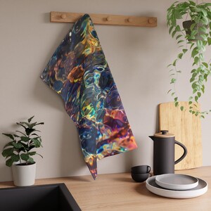 May include: A kitchen towel with a vibrant, abstract design resembling water reflections. The towel features a mix of blues, greens, yellows, and purples. It hangs from a wooden rack, adding a splash of color to the kitchen decor.