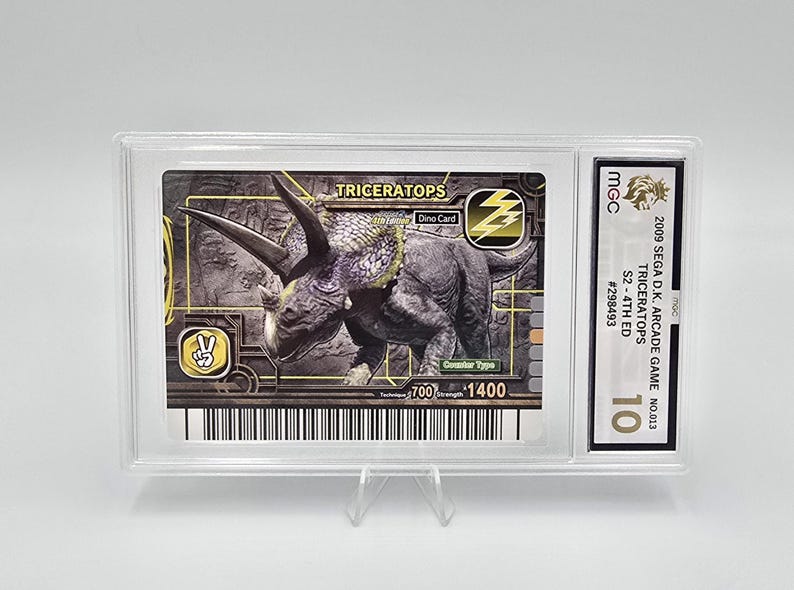 Puede incluir: Una tarjeta coleccionable calificada con un dinosaurio Triceratops del juego arcade Sega D.K. de 2009. La tarjeta est&aacute; dentro de un soporte de pl&aacute;stico transparente y tiene una calificaci&oacute;n de 10. El dise&ntilde;o de la tarjeta incluye la palabra "TRICERATOPS" y el texto "Dino Card".