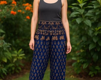 May include: A woman wearing a dark gray tank top and blue patterned pants. The pants have a repeating diamond and floral design in gold. The background is a green garden with orange flowers.