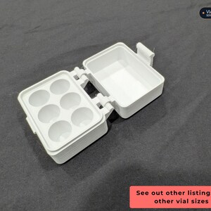 Op de afbeelding: Een witte plastic opbergdoos met een scharnierend deksel, voorzien van zes ronde uitsparingen aan de ene kant en een open vak aan de andere kant. De tekst VIAL STORAGE SERIES en See out other listings for other vial sizes is zichtbaar.