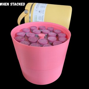 May include: A pink cylindrical container filled with multiple small glass vials topped with purple caps. Behind the container sits a yellow insulated bottle with a handle. The text STABLE WHEN STACKED is visible in the upper left corner.