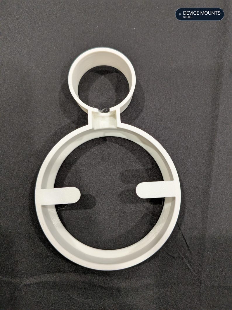 Puede incluir: Un soporte para dispositivo de pl&aacute;stico blanco que presenta un anillo circular grande con dos pesta&ntilde;as orientadas hacia adentro y un anillo m&aacute;s peque&ntilde;o unido a la parte superior. El texto "DEVICE MOUNTS SERIES" aparece en la esquina superior derecha.