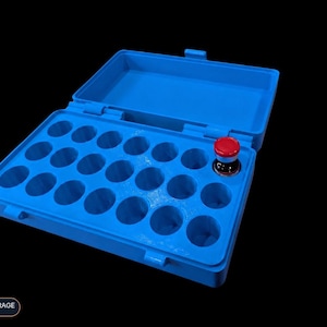 Op de afbeelding: Een felblauwe plastic opbergdoos met een scharnierend deksel, voorzien van eenentwintig ronde vakjes voor flesjes. E&eacute;n klein glazen flesje met een rode dop is in het vakje rechts geplaatst. De tekst VIAL STORAGE SERIES is in het beeld zichtbaar.