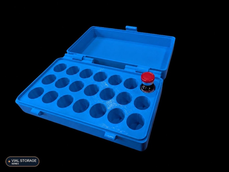Op de afbeelding: Een felblauwe plastic opbergdoos met een scharnierend deksel, voorzien van eenentwintig ronde vakjes voor flesjes. E&eacute;n klein glazen flesje met een rode dop is in het vakje rechts geplaatst. De tekst VIAL STORAGE SERIES is in het beeld zichtbaar.