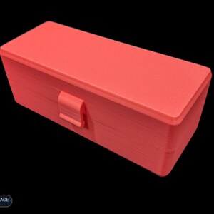 May include: A rectangular coral-colored storage box with a hinged lid and a central latch mechanism. The box features a textured surface consistent with 3D-printed construction. A small label in the corner displays the text VIAL STORAGE SERIES.