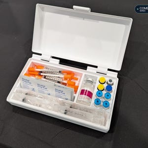 以下が含まれることがあります： COMBO STORAGE SERIESとラベルが貼られた白いプラスチック製の収納ケース。中には医療用品が入っており、オレンジ色のキャップが付いた注射器、アルコール綿、ピンクのラベルが付いたガラス瓶、青と黄色のキャップが付いた小さな小瓶が仕切りの中に収められています。