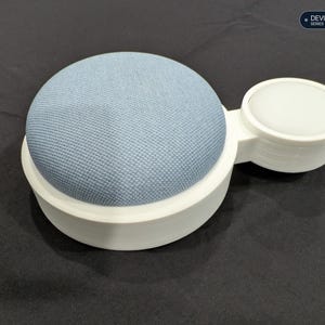 Puede incluir: Un altavoz inteligente cubierto de tela azul claro montado en un soporte circular de pl&aacute;stico blanco con una base circular blanca m&aacute;s peque&ntilde;a adjunta. El texto "DEVICE MOUNTS SERIES" es visible en la esquina superior derecha.