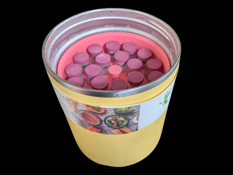 May include: A yellow cylindrical container with a metallic rim, holding a pink circular insert filled with numerous small glass vials topped with pink caps. A white label on the side features a photographic collage of various food items.