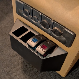 May include: A close-up of a black plastic panel with two toggle switches. The switches have blue and red buttons. The panel is mounted on a tan surface.