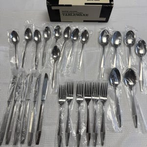 May include: A set of stainless steel tableware, including spoons, forks, and knives, packaged in clear plastic. The set includes a variety of utensils, with a box in the background that reads "MIRROR POLISHED STAINLESS STEEL TABLEWARE."