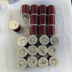 May include: A collection of metallic thread spools in a deep red color. The spools are labeled with the brand name "Dritz" and the text "METALLIC THREAD". Each spool contains 200 yards of thread, perfect for various crafting projects.