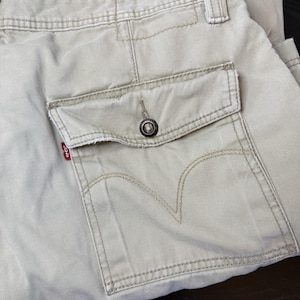 May include: Close-up of khaki-colored cargo pants featuring a button-down pocket and the Levi's brand tag. The pants have visible stitching and a classic design. The pocket has a button closure and the Levi's logo is visible.