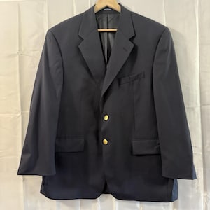 May include: A navy blue blazer with gold-colored buttons. The blazer has a classic two-button closure, notched lapels, and two front pockets. The garment is hanging on a wooden hanger against a white background.