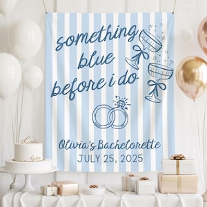 May include: A light blue and white striped banner with the text "something blue before i do" and "Olivia's Bachelorette JULY 25, 2025". The banner also features illustrations of champagne flutes and wedding rings. Balloons and gifts are in the background.