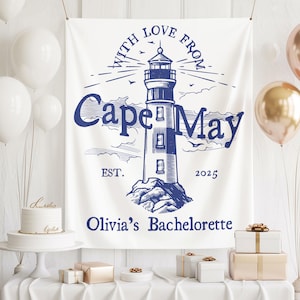 May include: A white fabric banner with a blue lighthouse illustration and text that reads "With Love From Cape May" and "Olivia's Bachelorette". The banner is decorated with balloons, gifts, and a cake.
