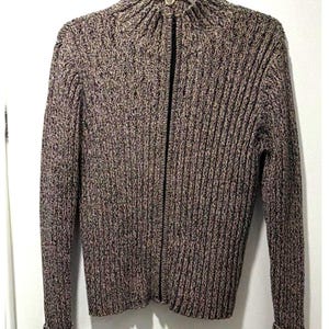 May include: A long-sleeve, full-zip jumper featuring a ribbed knit texture. The garment is crafted from a multi-coloured yarn blend, creating a speckled appearance with tones of black, white, and tan. It includes a high mock neck collar.