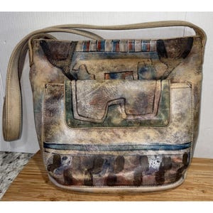 May include: A shoulder bag with a unique, abstract design. The bag features a flap pocket and a long strap. The color palette includes beige, brown, blue, and red, creating a vintage, artistic aesthetic. The bag is made of a textured material.