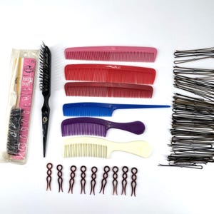 May include: A collection of hair styling tools, including a pink teasing brush, a black bristle brush, and several combs in pink, red, blue, purple, and cream. Also included are brown hair pins and a bundle of black bobby pins.