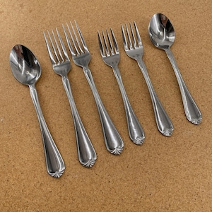 May include: A set of five pieces of stainless steel flatware consisting of two spoons and three forks. Each utensil features a polished silver finish and a decorative fan-shaped detail at the base of the handle, arranged in a diagonal row.