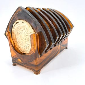 May include: A set of six brown and amber coasters with a matching holder. The coasters are arranged in a fan shape, and the holder has a curved design. The coasters are made of a dark, glossy material, and the holder has a swirled pattern.