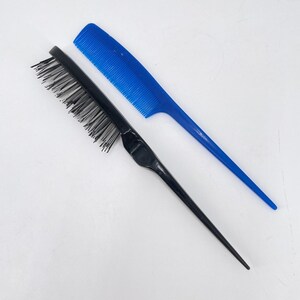 May include: Two hair styling tools on a white background. A black comb with bristles and a pointed handle is positioned next to a blue comb with a pointed handle. The blue comb has fine teeth.