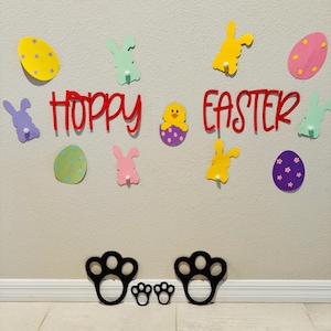 May include: A wall decorated with colorful paper cutouts of bunnies, eggs, and chicks. The words "Hoppy Easter" are written in red letters. There are also black paw prints on the floor.