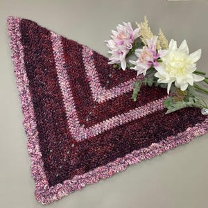 May include: A crocheted shawl in shades of burgundy, pink, and white with a scalloped edge.