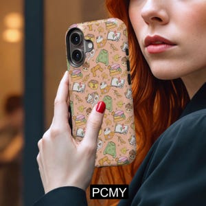 May include: A phone case with a repeating pattern of autumn-themed illustrations. The design includes books, sweaters, mugs, cats, and acorns in shades of beige, green, and brown. The text "PCMY" is visible at the bottom.