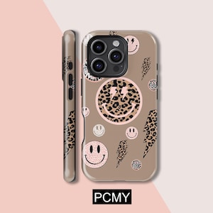 Könnte beinhalten: Eine beige Handyhülle mit einem sich wiederholenden Muster aus rosa Smiley-Gesichtern, Blitz-Symbolen mit Leopardenmuster und Kreisen mit Leopardenmuster. Die Hülle hat einen Kameraausschnitt und den Text "PCMY" unten.