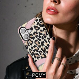 Peut inclure: Une coque de t&eacute;l&eacute;phone avec un motif l&eacute;opard. L'&eacute;tui pr&eacute;sente une bande rose, jaune et argent&eacute;e &agrave; paillettes. Le texte "PCMY" est visible en bas de l'&eacute;tui.