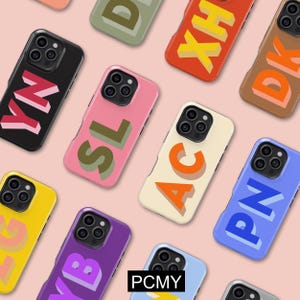 May include: A selection of vibrant phone cases, each displaying a different set of letters. Cases are in shades of black, pink, yellow, purple, blue, orange, and cream. Each case features a unique letter combination in a contrasting colour with a shadow.