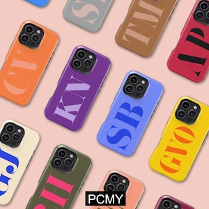 Puede incluir: Una colección de fundas de teléfono coloridas con varias iniciales en fuentes audaces y estilizadas. Las fundas son en tonos de naranja, morado, azul y amarillo. Las letras son de colores contrastantes, sobre un fondo rosa suave.