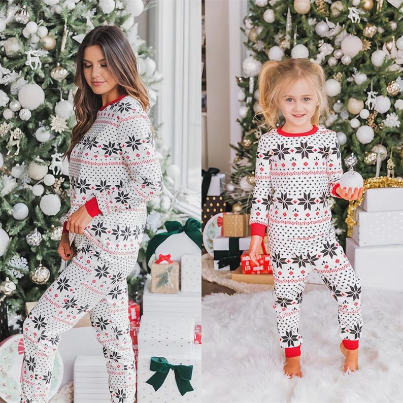 Puede incluir: Conjunto de pijamas navide&ntilde;os blancos a juego con un estampado de copos de nieve. Las camisetas y pantalones de manga larga tienen ribetes rojos en los pu&ntilde;os y el cuello. Los pijamas los llevan una mujer y una ni&ntilde;a peque&ntilde;a.