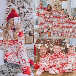 Puede incluir: Pijamas navide&ntilde;os rojos y blancos a juego con dise&ntilde;os de renos y copos de nieve. Los pijamas son usados por una familia de varias edades, incluyendo adultos y ni&ntilde;os. Una mujer lleva un gorro rojo y sostiene una taza de caf&eacute;.