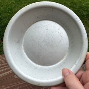 May include: A silver metal pie plate with a slightly raised rim and a smooth, shiny surface. The plate has visible scratches and signs of wear.