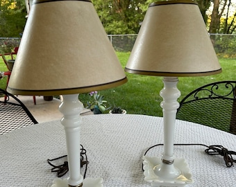 May include: Two white milk glass table lamps with scalloped bases and beige lampshades with brown trim.