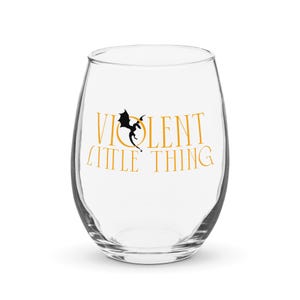 Op de afbeelding: Een helder, steelvrij wijnglas met de woorden "VIOLENT LITTLE THING" in gouden letters. Een zwarte draakafbeelding staat tussen de woorden. Het glas is leeg en staat op een wit oppervlak.