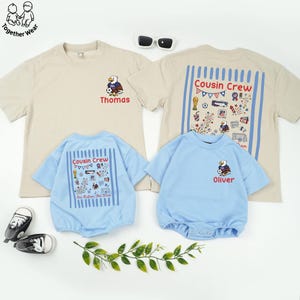May include: A collection of children's apparel, including two beige t-shirts and two light blue rompers. The t-shirts feature an eagle graphic and the name "Thomas" and "Oliver". The rompers have "Cousin Crew" text and patriotic illustrations.