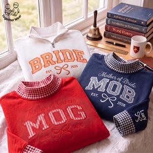May include: A white quarter-zip sweatshirt with orange gingham BRIDE EST. 2026 embroidery, a red sweatshirt with red gingham MOG EST. 2026 embroidery, and a navy sweatshirt with blue gingham MOB EST. 2026 embroidery and Lucy on the sleeve.