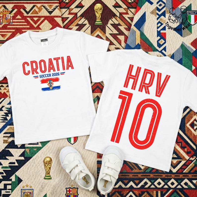 May include: Two white short-sleeved t-shirts. One shirt features the red text CROATIA, the text SOCCER 2026, and a Croatian flag graphic. The other shirt displays the red text HRV and the number 10. A pair of white sneakers is placed below the shirts.