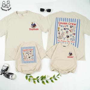 May include: Beige t-shirts and rompers with soccer-themed graphics. The shirts feature an eagle mascot and the names "Thomas" and "Oliver." The rompers and one shirt display "Cousin Crew" and "One Nation, One Team" text.
