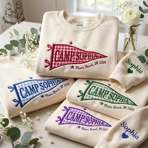 May include: Cream-colored sweatshirts and matching cuffs embroidered with "Camp Sophia" pennants in various colors, including red, blue, green, and purple. Each pennant has the text "Miami Beach, FL 2026" and star accents. The cuffs are embroidered with the name "Sophia".